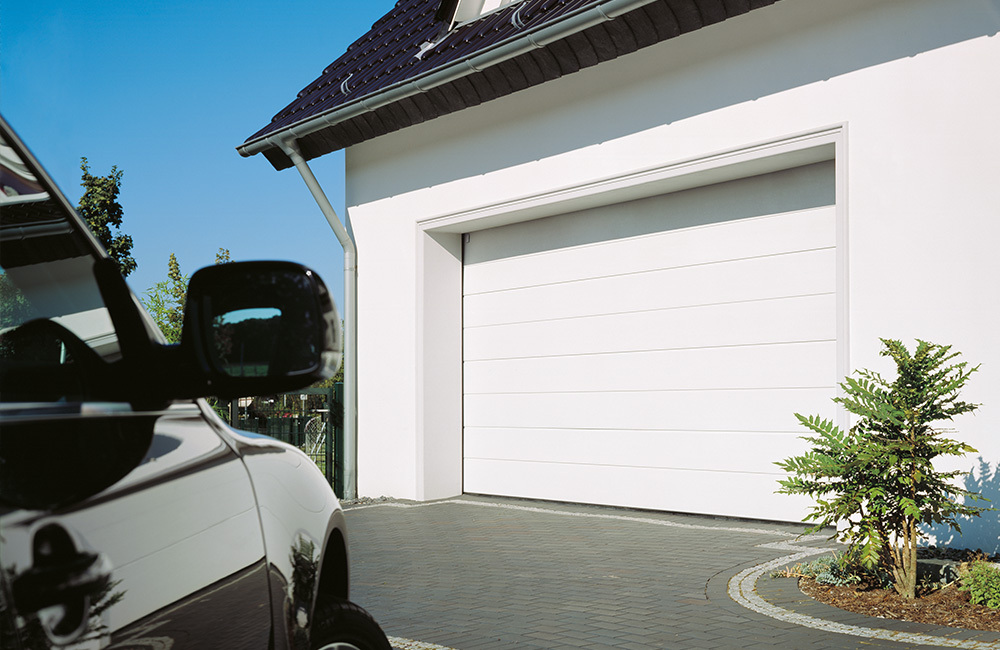 CarTeck sectional garage door in white next to a car on a driveway.